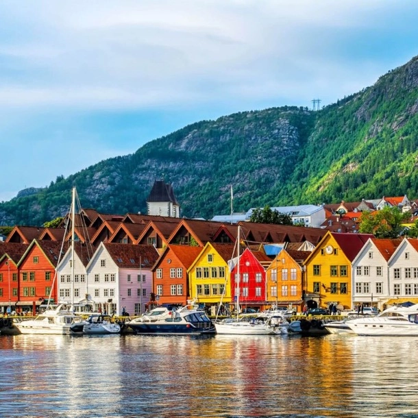 The image shows a row of colorful buildings by a waterfront, with boats docked in front and a hill in the background. This scene is interesting for its vibrant architecture and picturesque setting, which suggests a coastal town likely popular with tourists.
